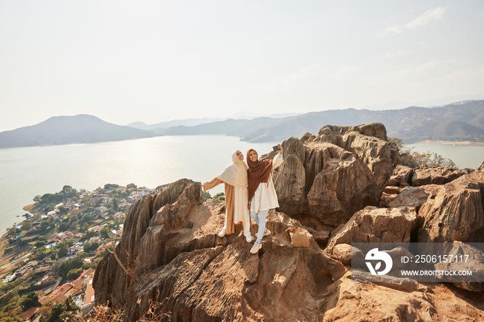 Smiling young friends taking selfie with smartphone on top of rock