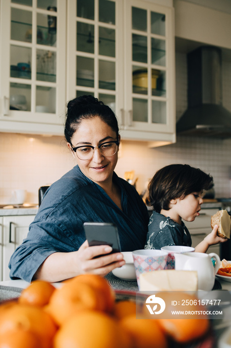 Smiling mother with son using smart phone at dining table during breakfast