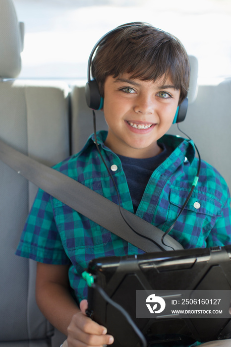 Portrait happy boy with headphones and digital tablet in car