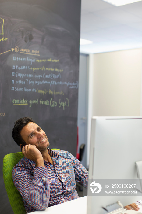 Smiling businessman talking on smart phone at computer