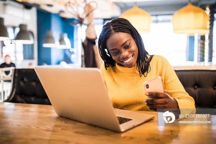 Lifestyle and people concept. Portrait of happy young african woman in a coffee shop using mobile ph