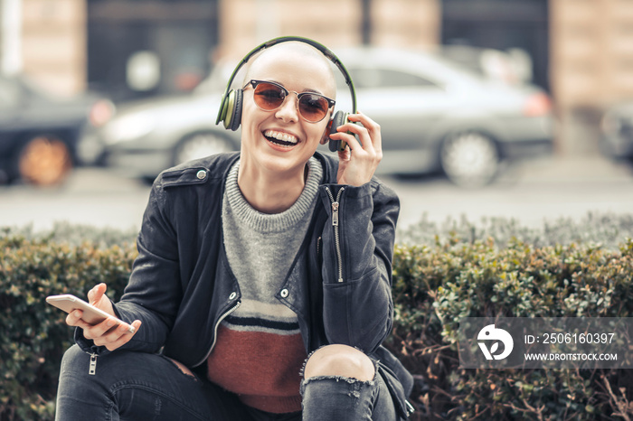 Young modern woman with bald hairstyle listening to her favorite music over her big green headphones