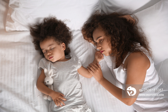 Little African-American girl with mother sleeping in bed at night