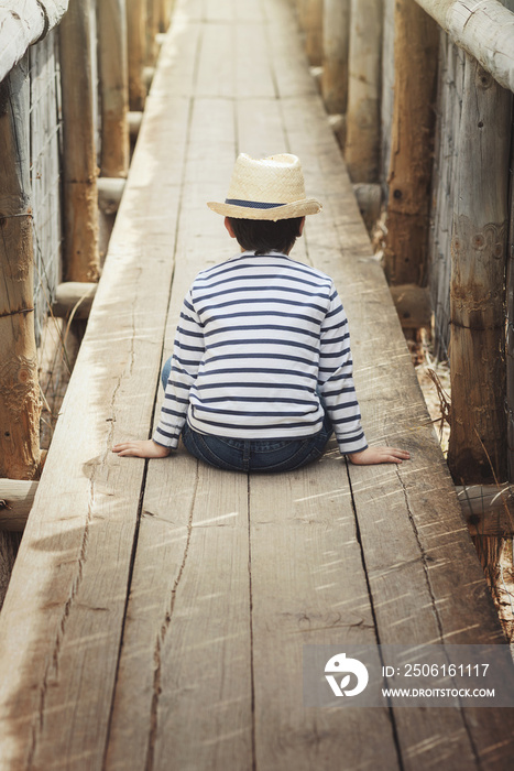 niño triste y pensativo sentado sobre un puente de madera