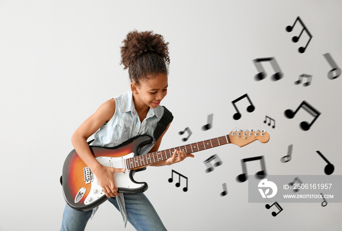 African-American girl playing guitar against light background