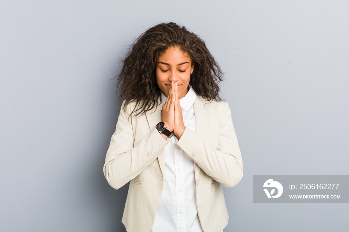 Young african american business woman holding hands in pray near mouth, feels confident.