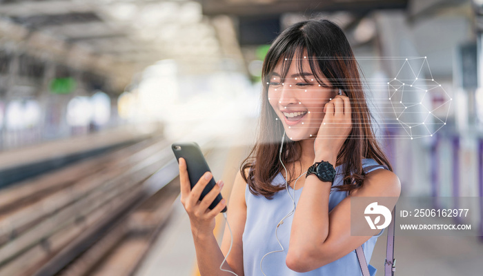 Asian woman using face recognition via smart mobile phone and listening the music at Railroad Statio