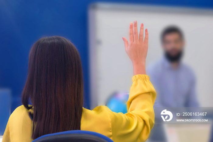 女学生坐在课堂上，在讲座中举手提问的后视图。