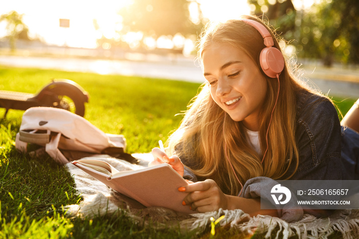 女孩在外面的自然绿色公园里，戴着耳机听音乐。