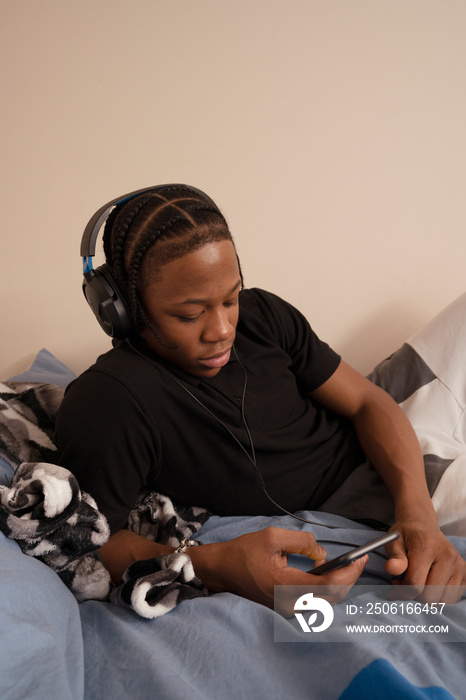 Teenage boy listening to music on bed at home