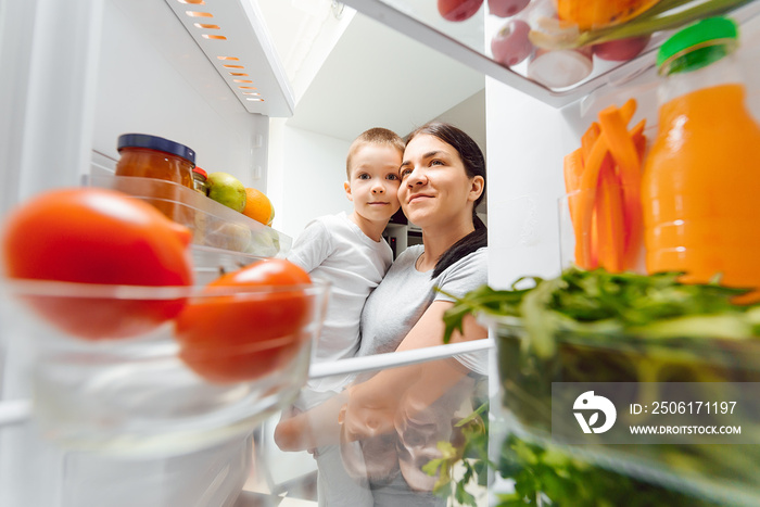 Mother with her baby opening refrigerator at kitchen