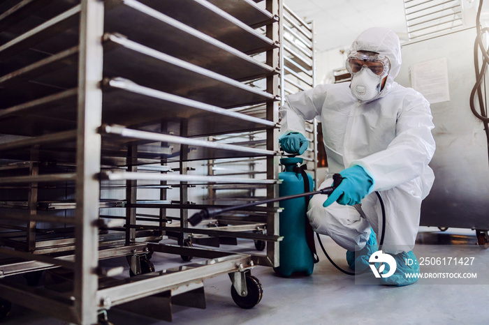 Man in protective suit and mask disinfecting warehouse full of food products from corona virus / cov