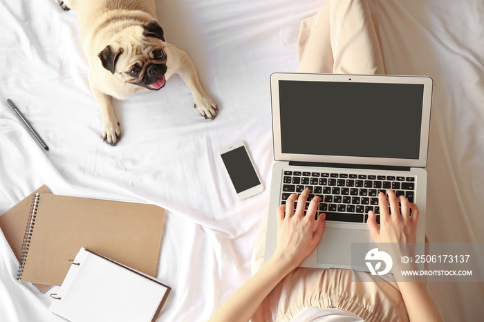 Young woman with laptop and cute pug dog resting on bed