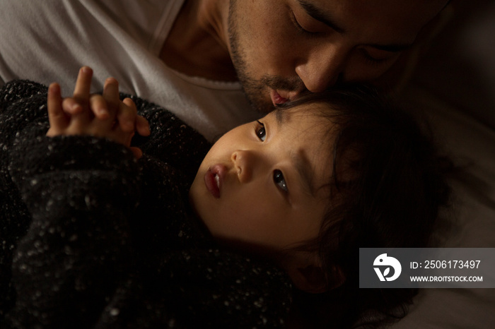 High angle view of loving father kissing thoughtful daughter lying on bed at home