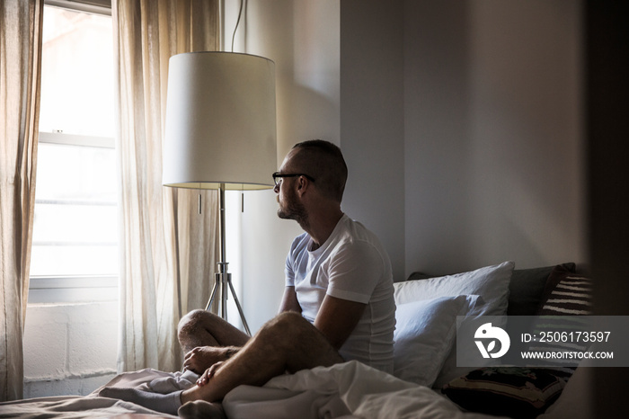 Man sitting on bed and looking through window