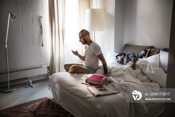 Man using smartphone besides his partner sleeping on bed