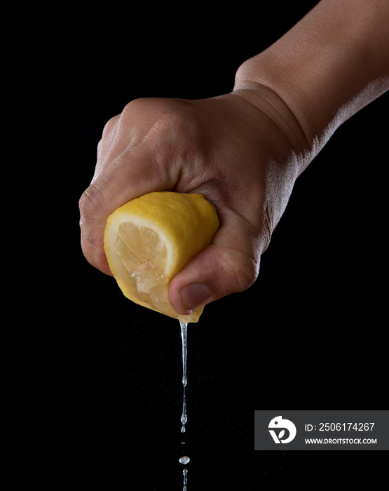 Female hand squeezing half of lemon on black background