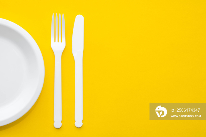 黄色背景的塑料白色叉子、刀和盘子。烹饪用具。俯视图。极简风格