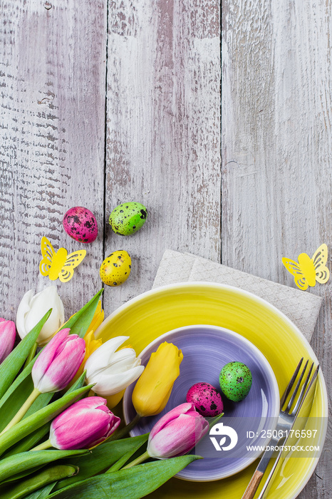 节日春天背景。复活节餐桌上摆放着春天的郁金香、五颜六色的鹌鹑蛋和餐具