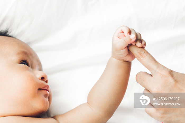 Baby hand holding mothers finger on white bed.Love of family and baby protection concept