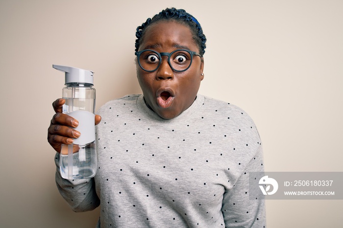 Young african american plus size sportswoman with braids drinking bottle of water scared in shock wi