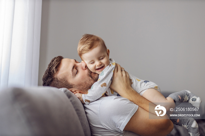 Adorable little blond boy playing with his caring father and biting his nose. Father is smiling.