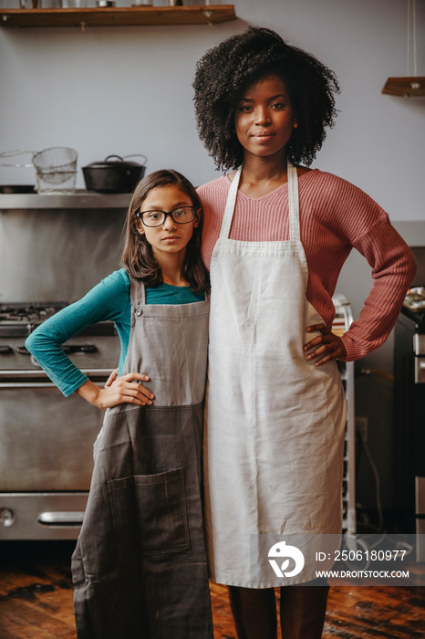 Portrait of confident female chef with cute student standing against wall in training class