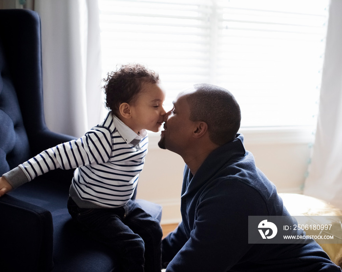 Side view of cute son kissing on fathers nose while sitting against window at home