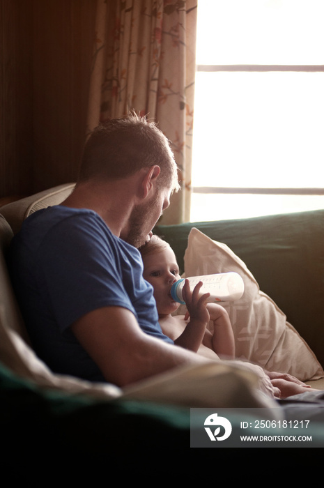 Father sitting with baby son (12-17 months) on sofa