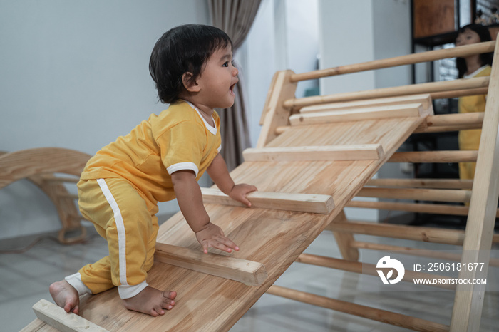 baby girl climbing up in pikler triangle toys in the living room background