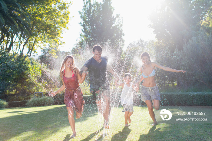 Playful family running through sprinkler in sunny summer backyard