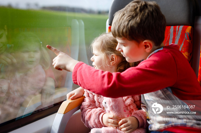 可爱的蹒跚学步的小女孩和弟弟坐在火车上看着窗外。两个可爱的