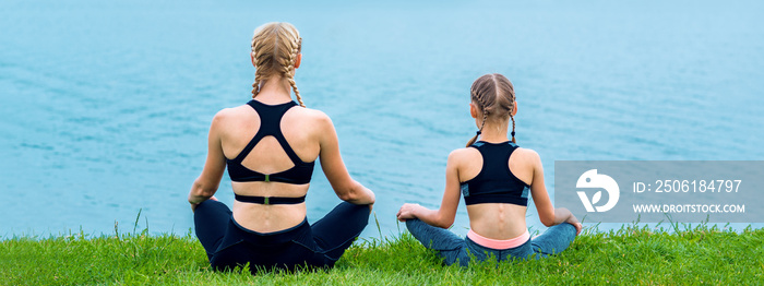 母亲和女儿在湖岸的草地上做瑜伽练习。