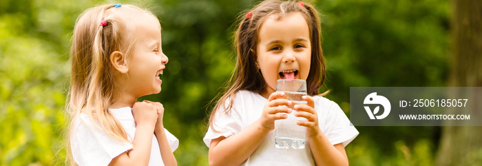 Two little girl carrying a transparent glass of fresh water in a green widow. Concept of purity, eco