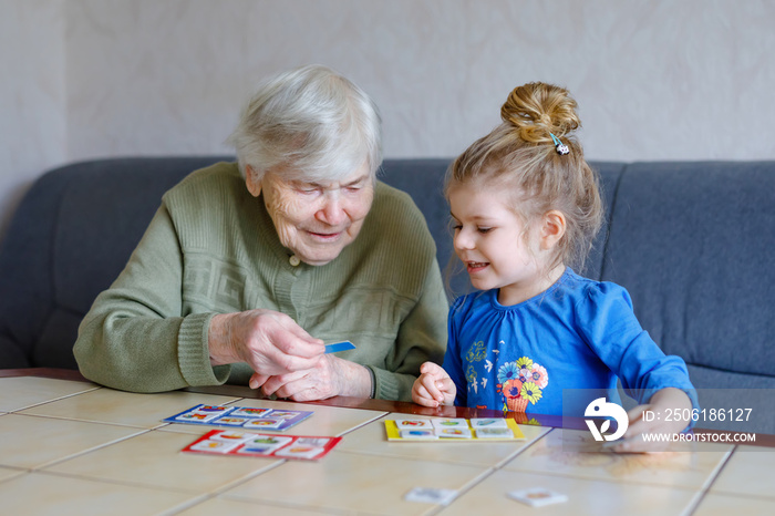 Beautiful toddler girl and grand grandmother playing together pictures lotto table cards game at hom