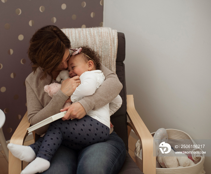 High angle view of happy mother tickling cute daughter while sitting on chair against wall at home