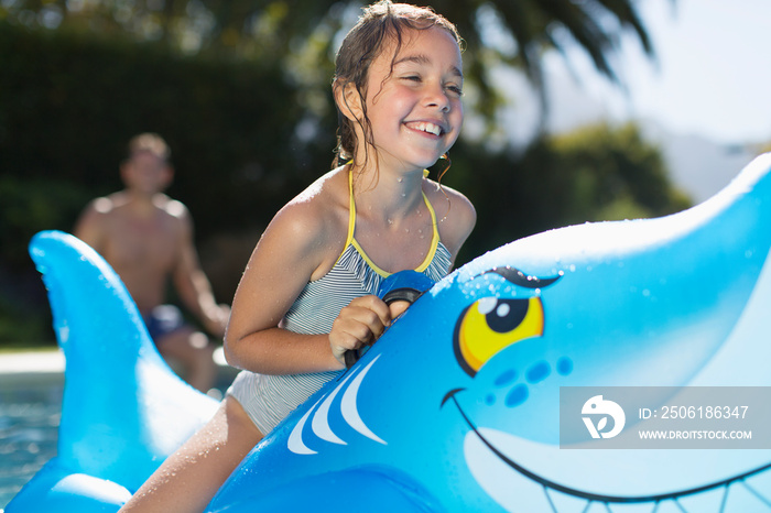 Happy girl on inflatable shark in sunny swimming pool