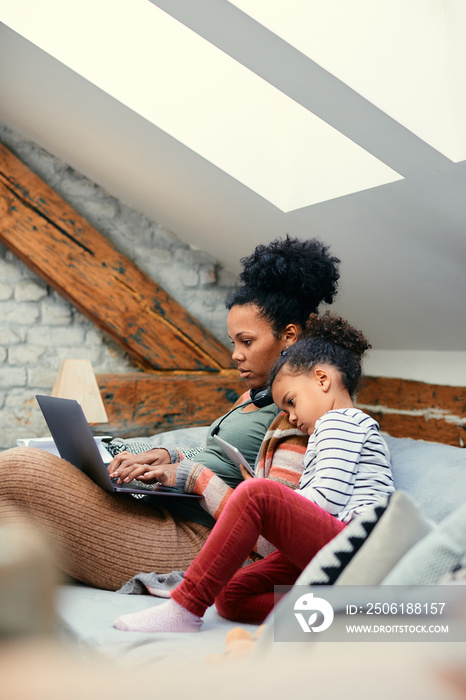 Bored black girl uses touchpad while her mother is working on laptop at home.