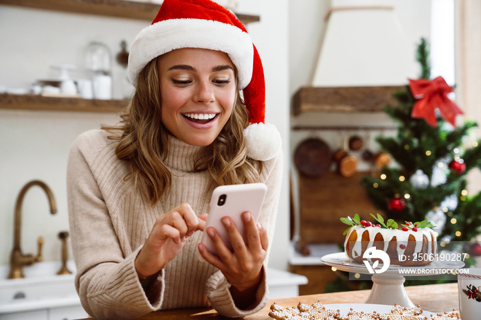 Happy woman in santa claus hat smiling while using mobile phone