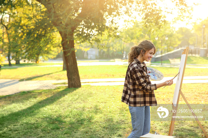 Young female artist painting picture in autumn park