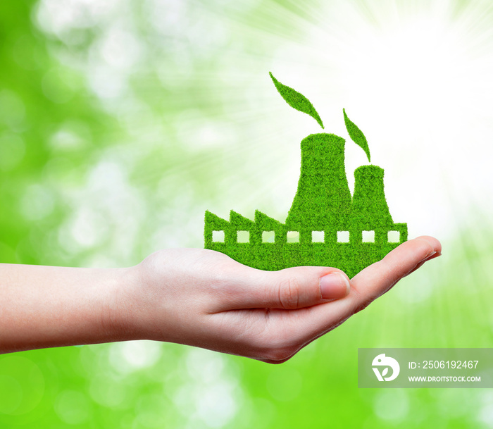 Nuclear power plant icon in hand on green natural background.