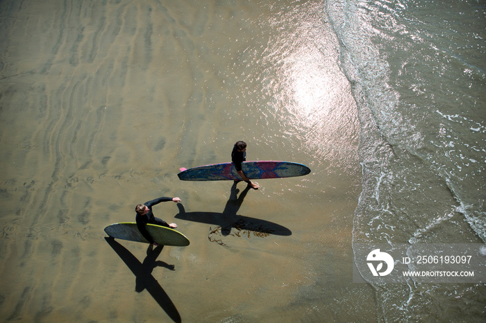 Two men walking with surfboards on beach