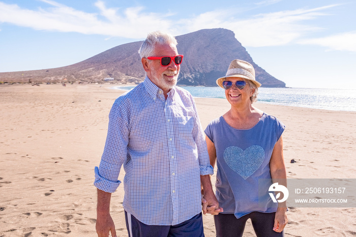 couple of mature old people having fun walking on the sand of the beach together enjoying their vaca