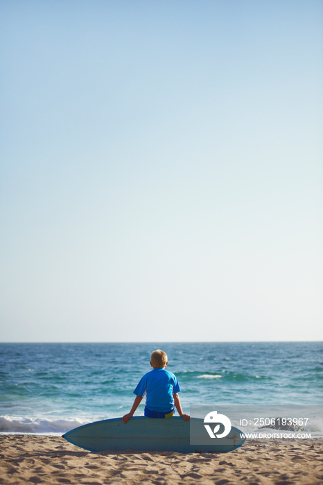 Boy (8-9) sitting on surfboard on beach