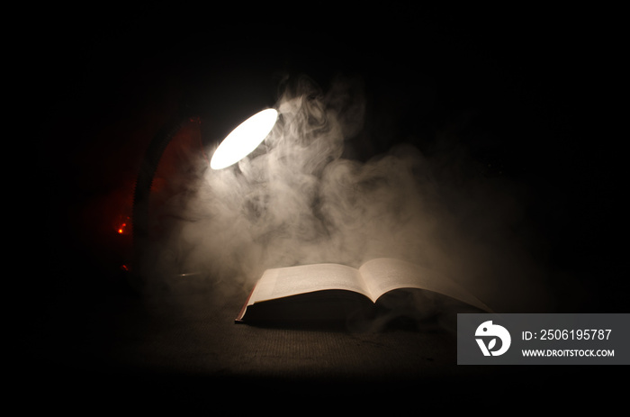 Open book near glowing table lamp on dark background, Lamp and opened book with smoke on background.