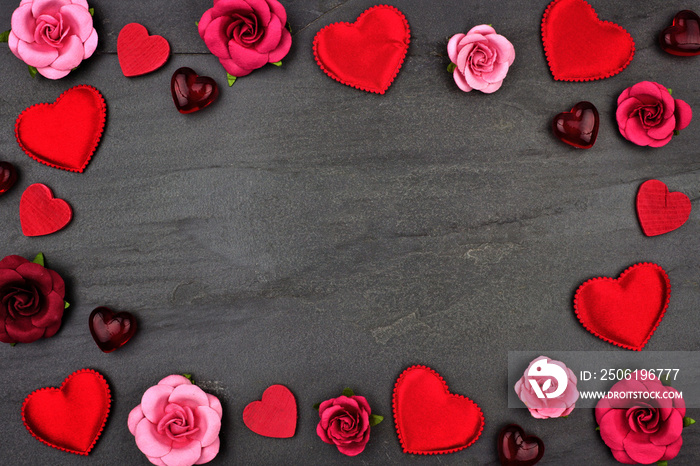 Valentines Day frame of hearts, flowers and decor against a dark stone background with copy space