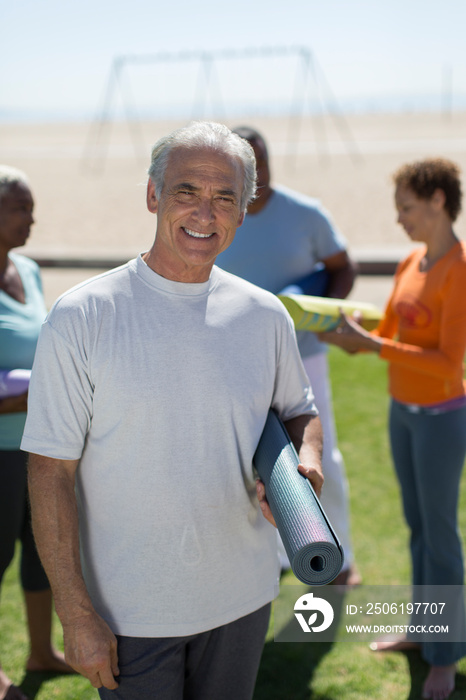 Portrait happy senior man with yoga mat on sunny beach grass