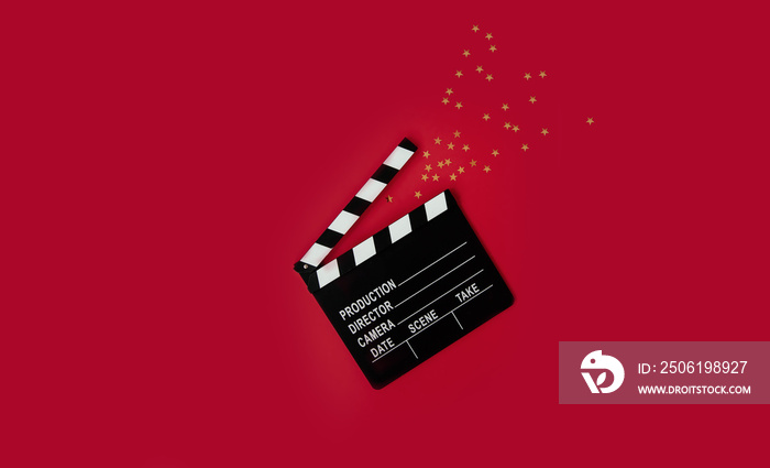 open clapperboard with gold stars confetti on a red background. copy space. concept of cinemas, film