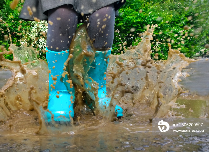 穿着蓝色雨靴的孩子跳进水坑