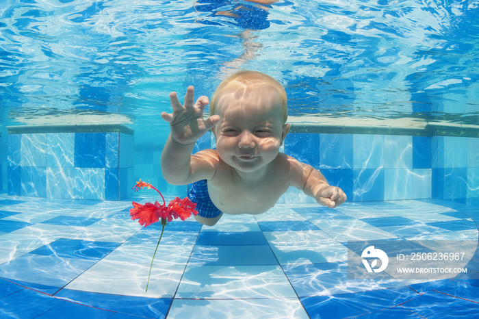 微笑的小男孩在水下潜水，为蓝色的水池里的红花欢乐